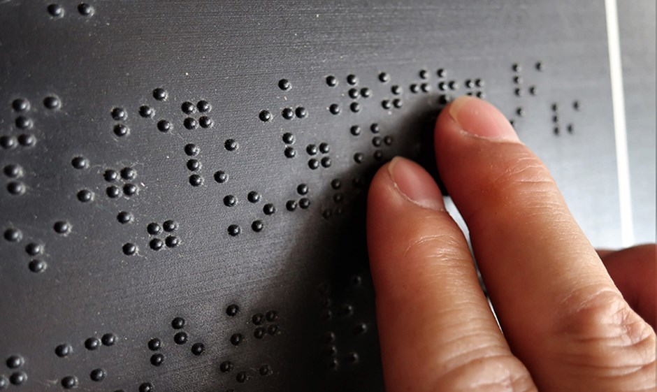 Two fingers touching a black surface with braille on it.