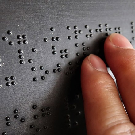 Two fingers touching a black surface with braille on it.