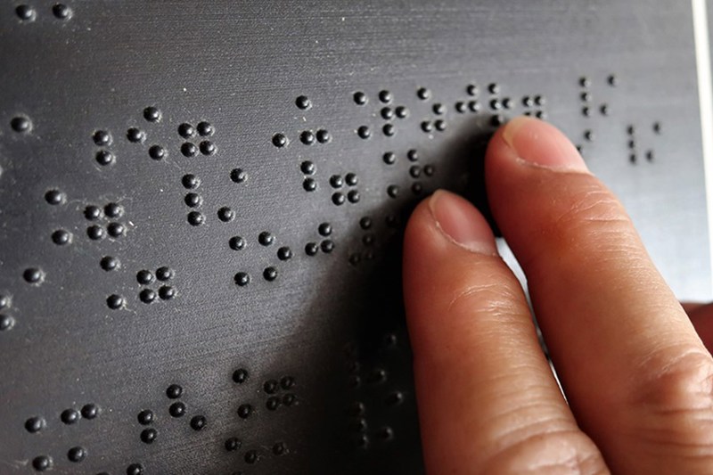 Two fingers touching a black surface with braille on it.