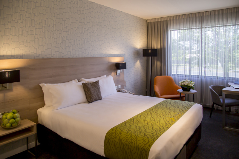 Large bed with side table, sofa lounge chairs and table with lamp in corner.