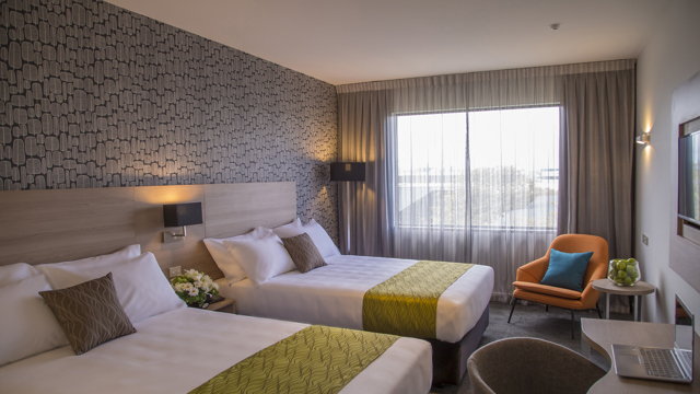 Two large beds with side tables, sofa lounge chair and desk and chair with lamp in corner.