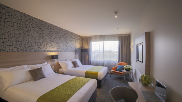Two large beds with side tables, sofa lounge chair and desk and chair with lamp in corner.