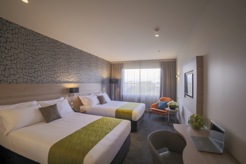 Two large beds with side tables, sofa lounge chair and desk and chair with lamp in corner.