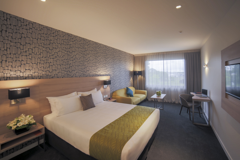 Large bed with side table, sofa, table, flatscreen TV, desk and chair with lamp in corner.