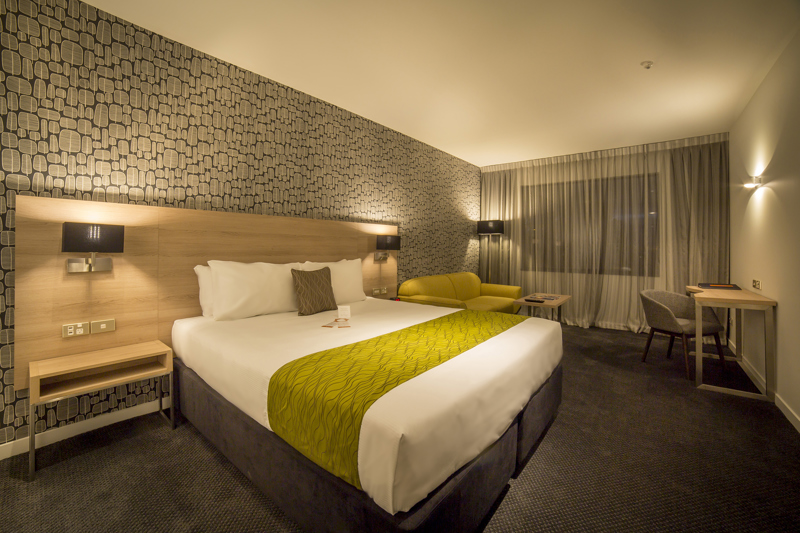 Luxury room with large bed, side table, sofa, table, flatscreen TV, desk and chair with lamp in corner.