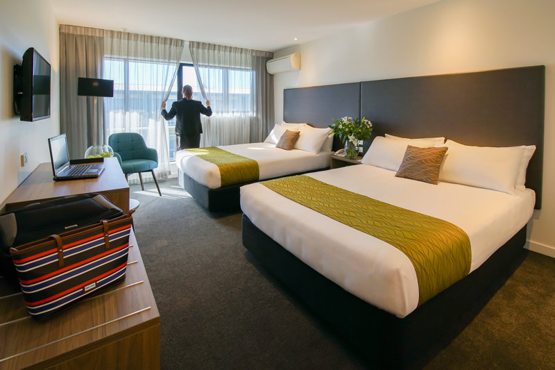 Two large beds with lounge chair, desk and table, TV and lamp in corner.