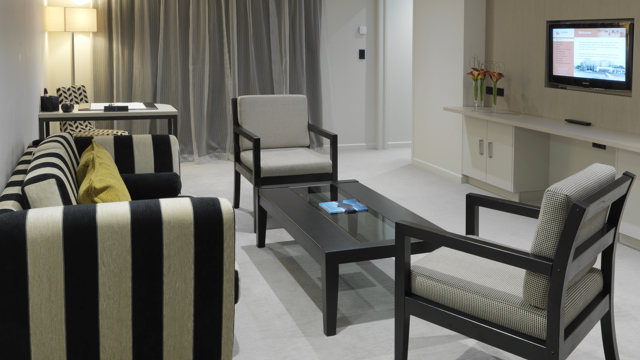Lounge area of executive suite with sofa, chairs, coffee table, flatscreen, desk, chair and lamps.
