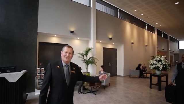 Older customer service man greeting hello and extending arm in welcoming gesture.
