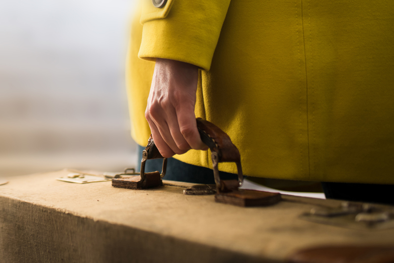 Close up of woman in yellow coat carrying a quality suitcase.