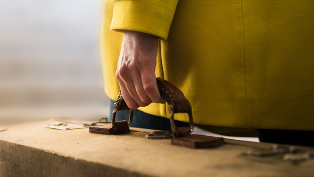 Close up of woman in yellow coat carrying a quality suitcase.