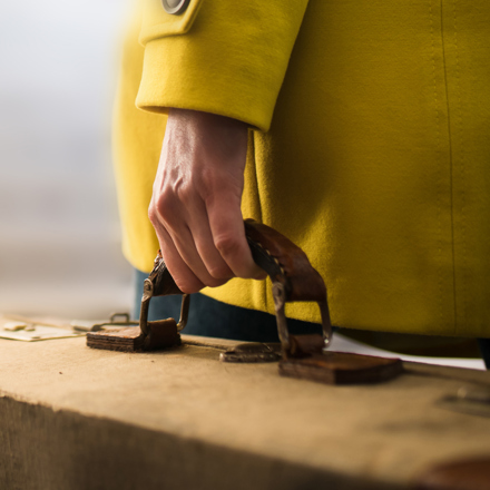 Close up of woman in yellow coat carrying a quality suitcase.