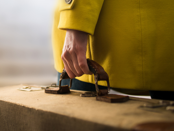 Close up of woman in yellow coat carrying a quality suitcase.