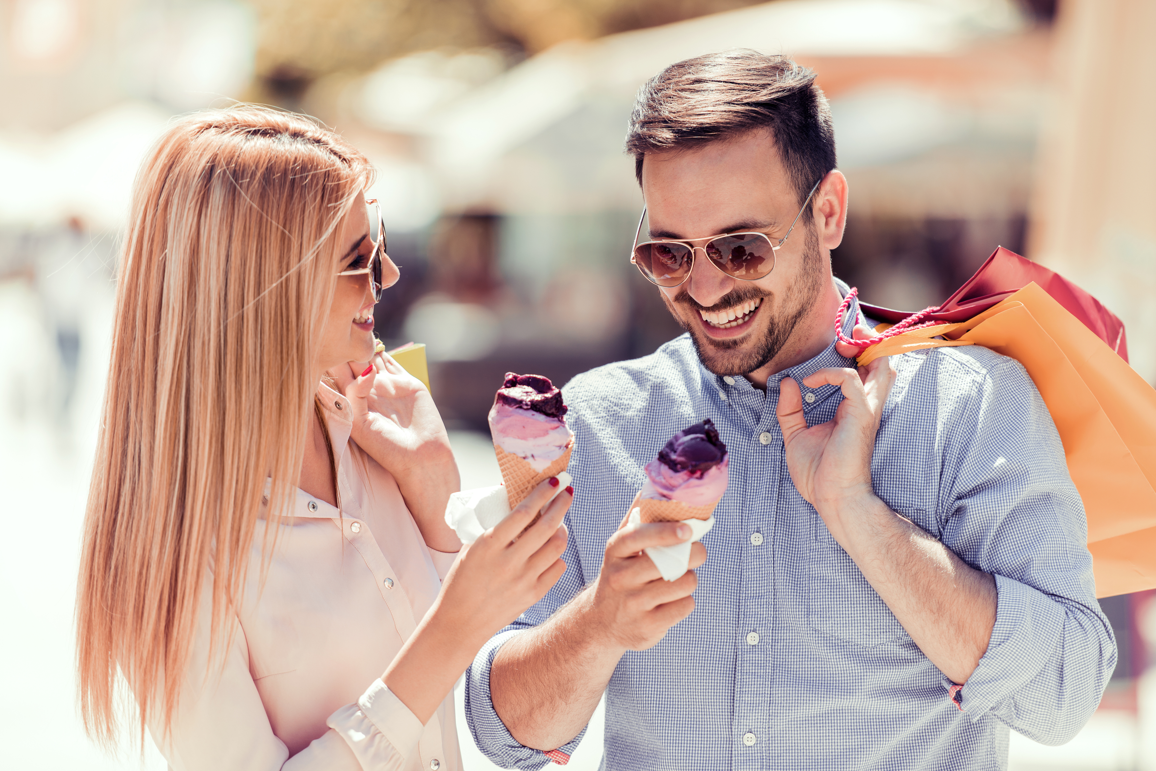 Couple wearing sunglasses, eating ice cream and holding shopping bags.