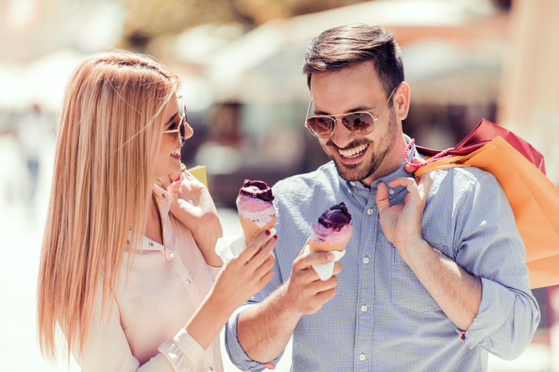 Couple wearing sunglasses, eating ice cream and holding shopping bags.