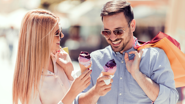 Couple wearing sunglasses, eating ice cream and holding shopping bags.
