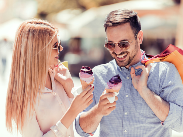 Couple wearing sunglasses, eating ice cream and holding shopping bags.