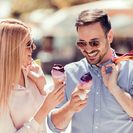 Couple wearing sunglasses, eating ice cream and holding shopping bags.