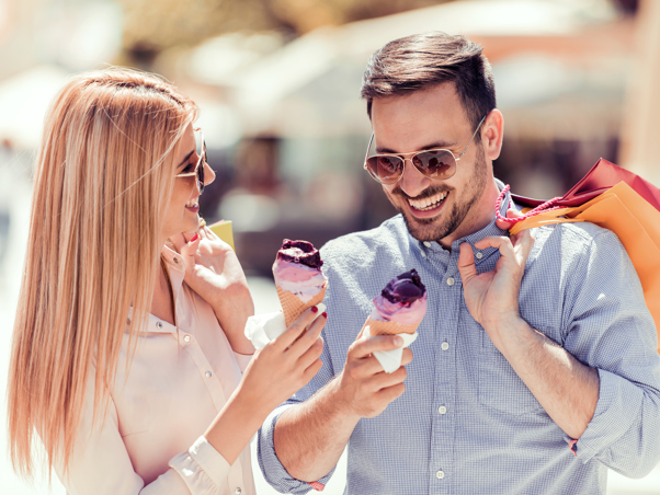 Couple wearing sunglasses, eating ice cream and holding shopping bags.