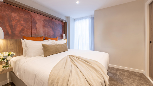 Luxury king bed with luxury linen and furnishings including flatscreen on wall and art on headboard. 
