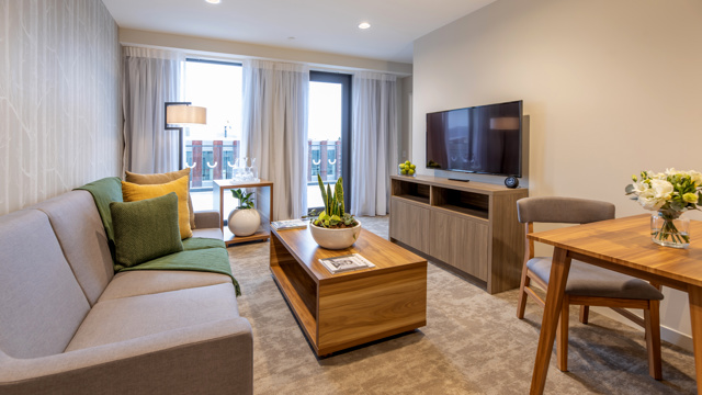 Lounge space with sofa, dining table and chairs, coffee table in centre, flatscreen on wall with floor to ceiling window.