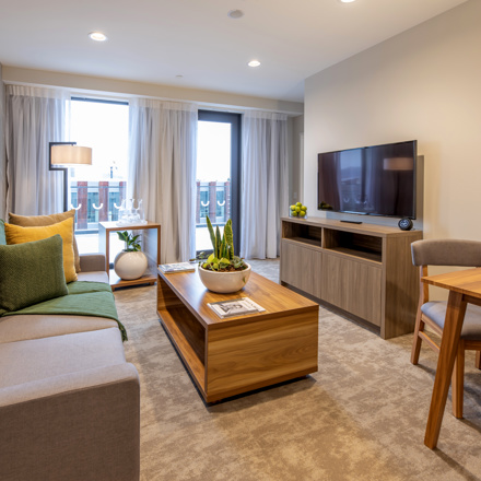 Lounge space with sofa, dining table and chairs, coffee table in centre, flatscreen on wall with floor to ceiling window.