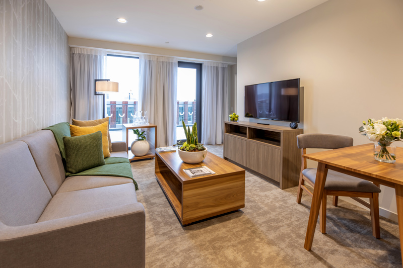 Lounge space with sofa, dining table and chairs, coffee table in centre, flatscreen on wall with floor to ceiling window.