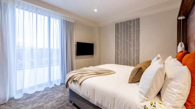 Luxury king bed with luxury linen and furnishings including flatscreen on wall and art on headboard. Floor to ceiling window. 