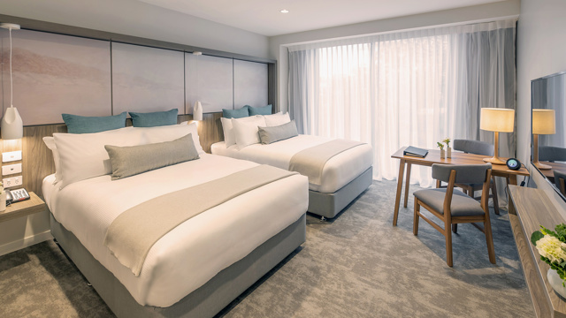 Two large beds with luxury linen. Large floor to ceiling window with TV, lamps, table and chairs