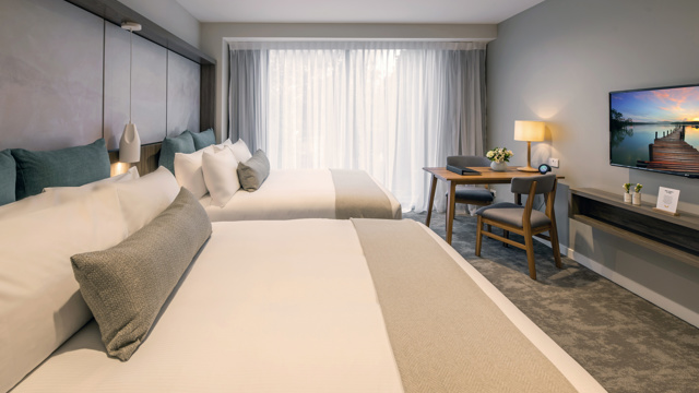 Two large beds with luxury linen. Large floor to ceiling window with TV, lamps, table and chairs