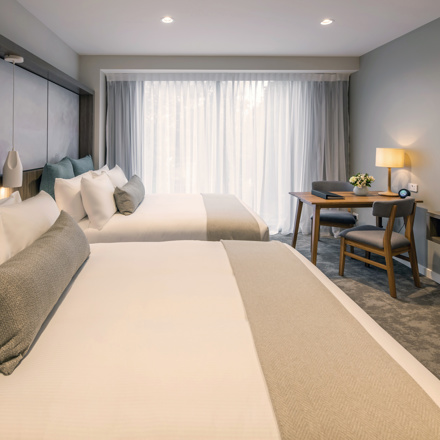 Two large beds with luxury linen. Large floor to ceiling window with TV, lamps, table and chairs