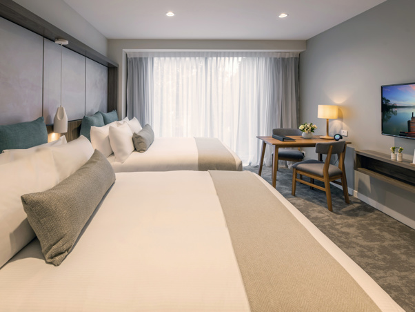 Two large beds with luxury linen. Large floor to ceiling window with TV, lamps, table and chairs