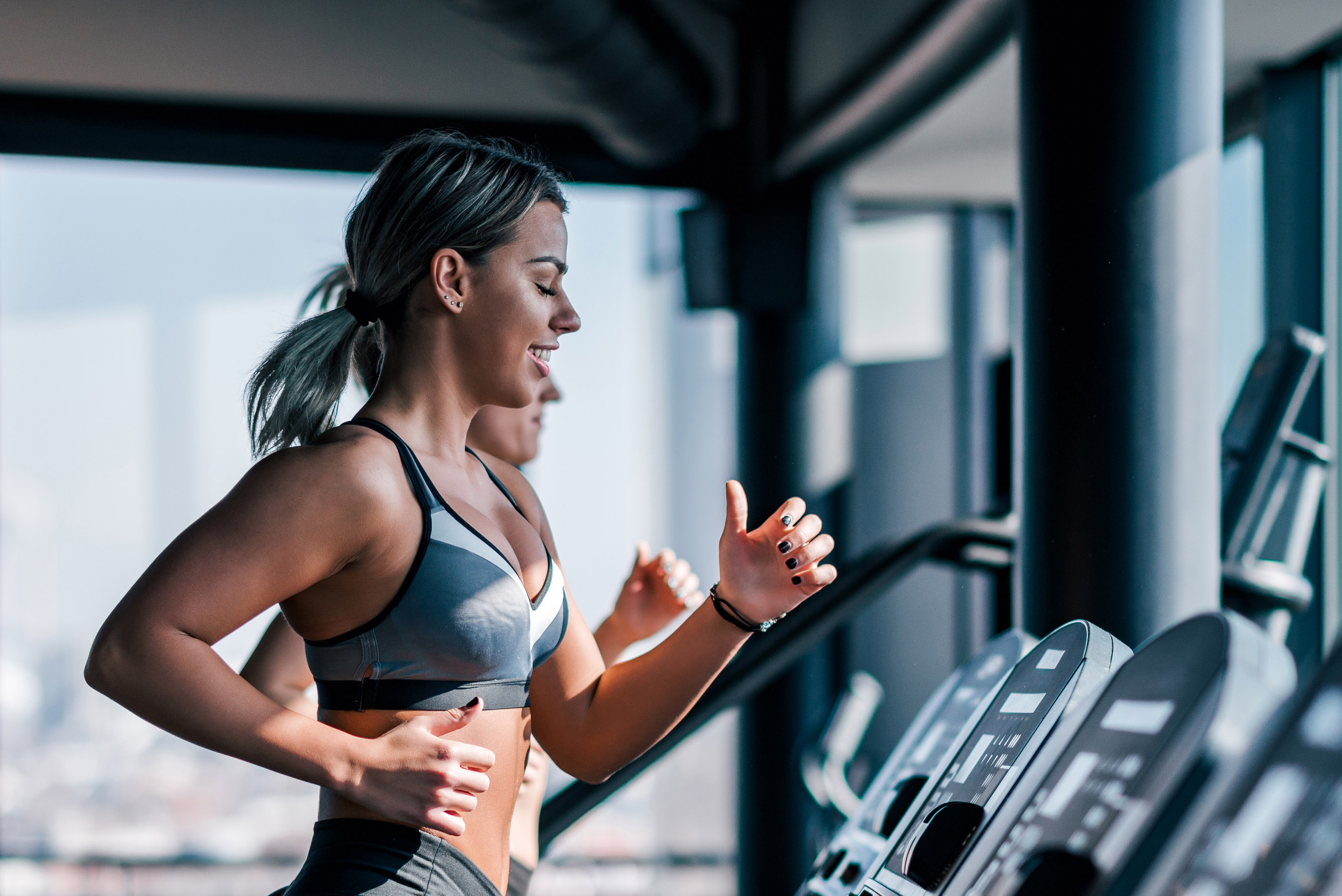 Two girls running on treadmill be a window.