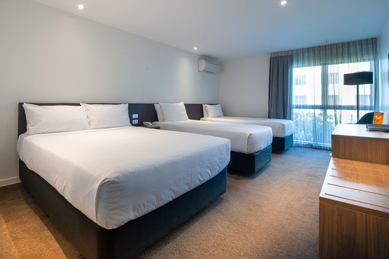 Triple beds with side table, desk and chair and lamp in corner.