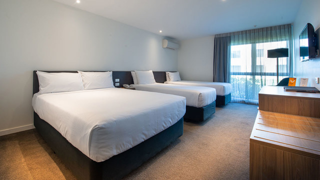 Triple beds with side table, desk and chair and lamp in corner.
