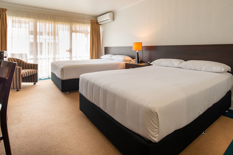Two beds with lounge chair, TV, lamps, desk and chair.