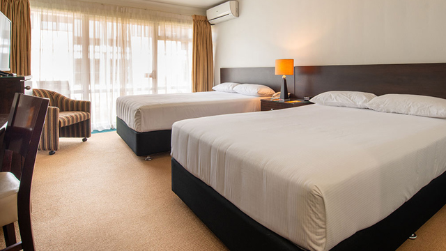 Two beds with lounge chair, TV, lamps, desk and chair.